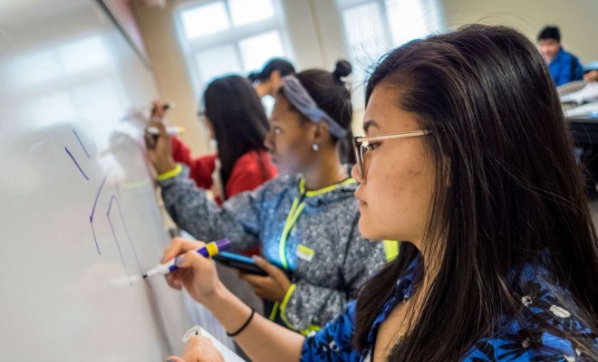 Students in Chinese class writing characters on a whiteboard.