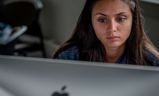 Close view of a woman's face as she looks at a monitor which is in the foreground.