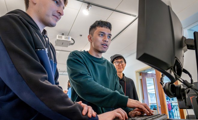 Three men are pictured looking at a computer screen intensely. 