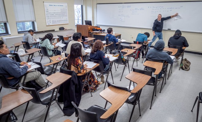 Professor teaching in front of a whiteboard to a classroom full of students. 