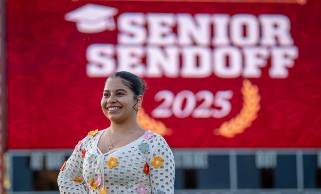 Angela Castro stands in front of a large red sign with white lettering that says Senior Sendoff 2025.