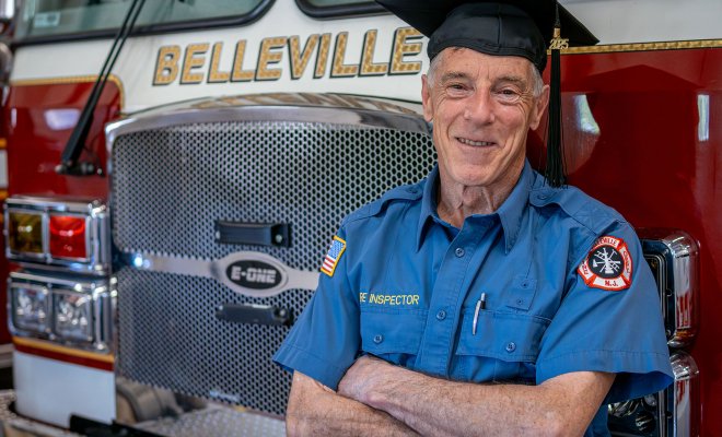 Ralph Castellano celebrates his Montclair State University graduation at the Belleville Fire Department, wearing his uniform and graduation cap.