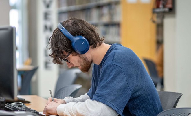 Student with headphones sitting at a computer in the library.
