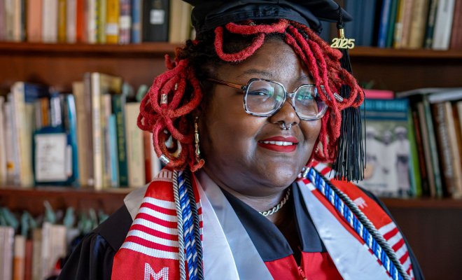 Khara Brown wears her cap and gown for a photograph taken next to a bookshelf inside Coder House, home to the Center for Heritage and Archaeological Studies.