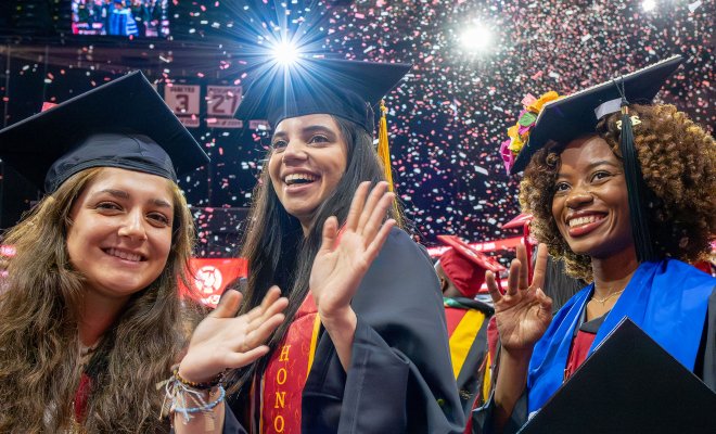 Three graduates in caps and gowns smiling with confetti falling around them