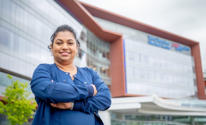 Woman in front of a hospital with her arms crossed, smiling. 