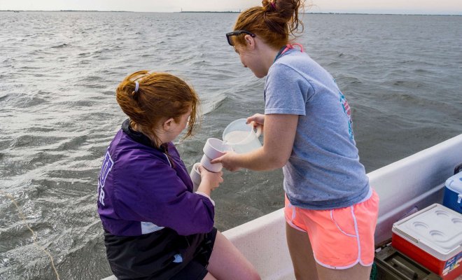 Two students on a boat collect a sample of ocean water.