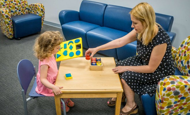 Sitting at a low table, a woman and a young girl play with colored blocks.