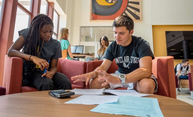 Two students in the CELS atrium collaborate on homework with the aid of a calculator.