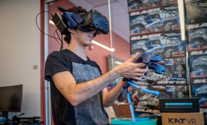Student using VR headset with two controllers in front of a wall of remote controlled cars.