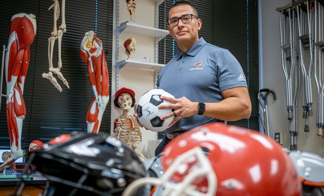 Luis Torres holds a soccer ball in a classroom filled with sports equipment.