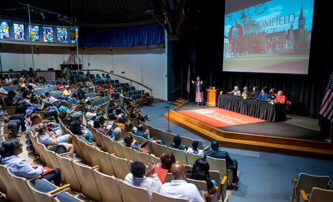 An orientation is taking place in an auditorium with a projector and stage.
