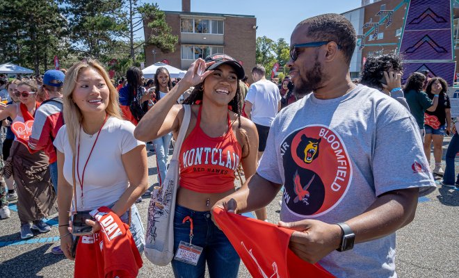 Two Montclair State University students and one Bloomfield College student stand together, chatting at an outdoor carnival.
