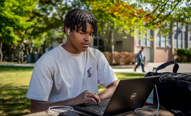 Student on his laptop on a table outside. 