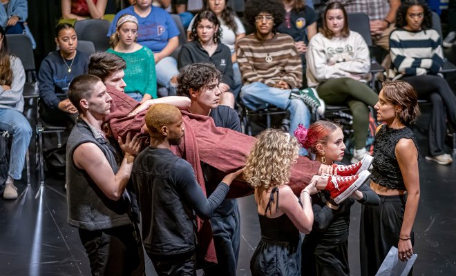 Five actors carry an actor wrapped in cloth as the audience during a performance of Richard III.