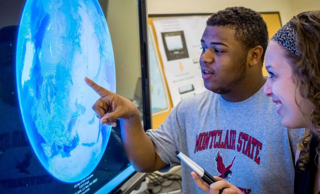 Two students standing in front of an interactive display using Google Earth.