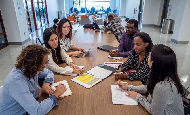 Students in discussion with notebooks and textbooks on a table.