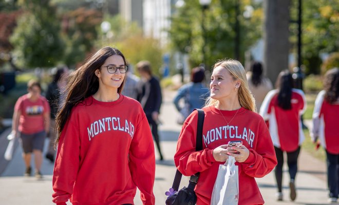 Two students in red sweatshirts walk on campus.