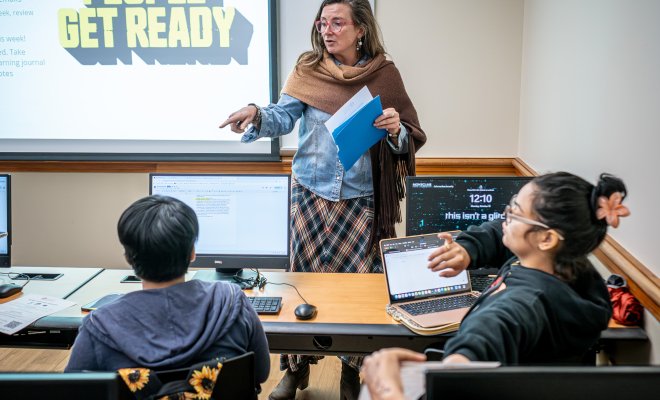 Woman teaching in front of a class with students sitting in front of her. 