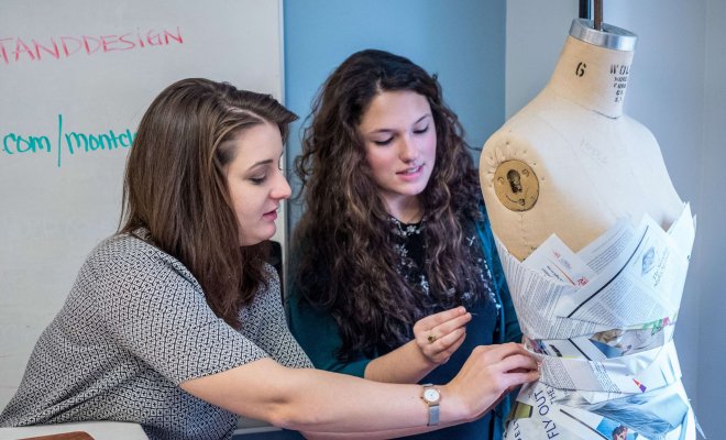 Two students shaping a garment made of newspaper on a manikin.