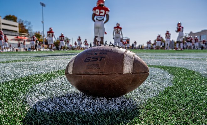 Football on the field. Football players are in the background getting ready for practice.