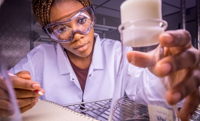 woman student staring intensely at a flask filled with plant matter.