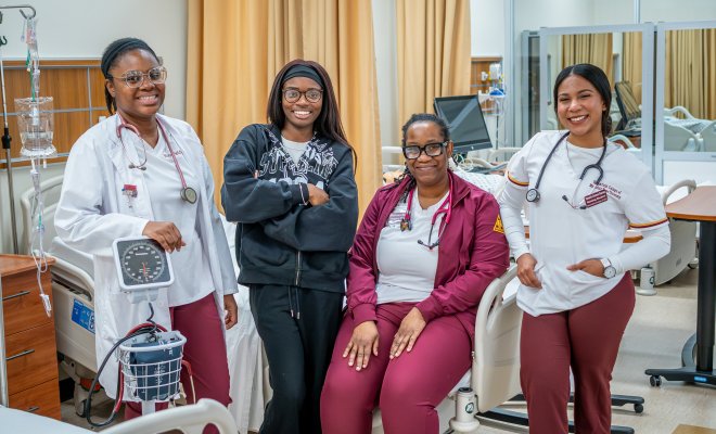 Four women smiling at the camera with their scrubs and nursing gear on. 