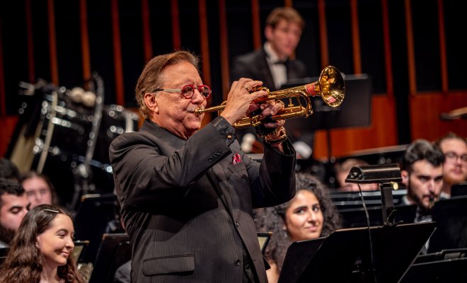 Arturo Sandoval plays the trumpet with students in the University Wind Symphony seated behind him.