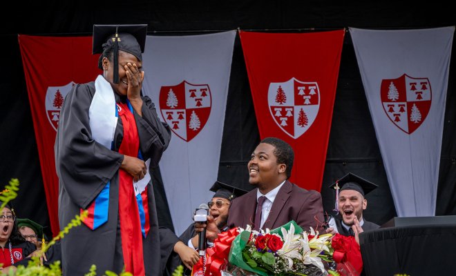 Man in cap and gown on stage proposing to woman in cap and gown