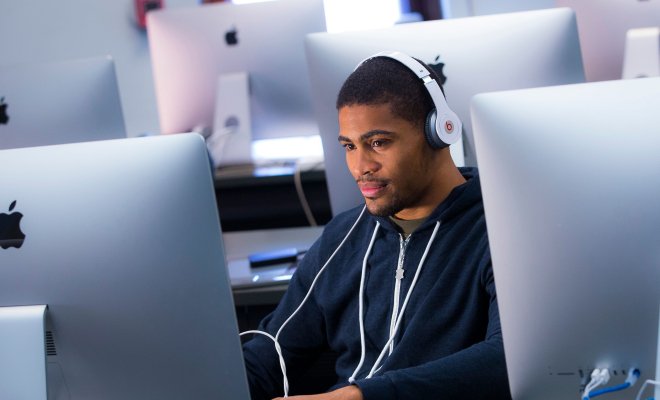 Student wearing headphones while using large-screen computer in computer lab