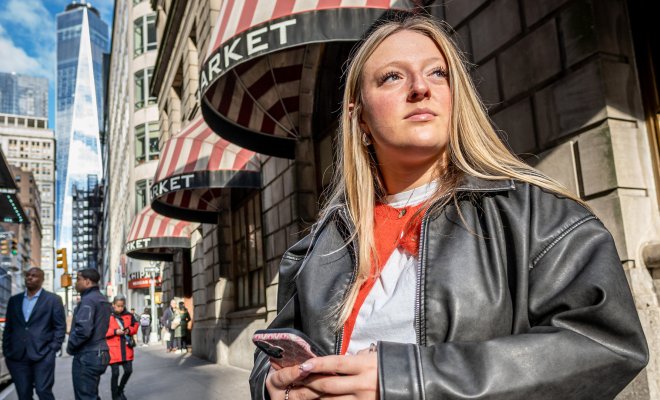 Emma Haskell stands on a sidewalk in lower Manhattan holding her phone.