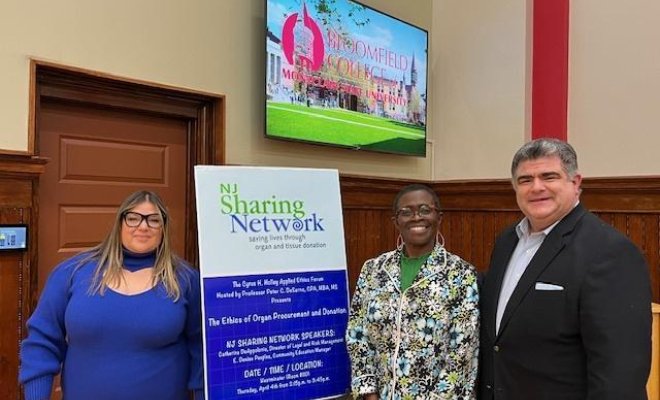 Three people are standing in front of a poster. 