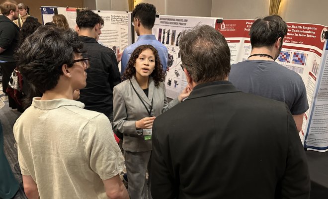 Woman pictured explaining a poster to two other gentleman. 