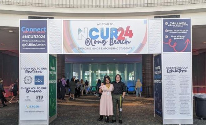 Two students are under the posters for the NCUR 2024.