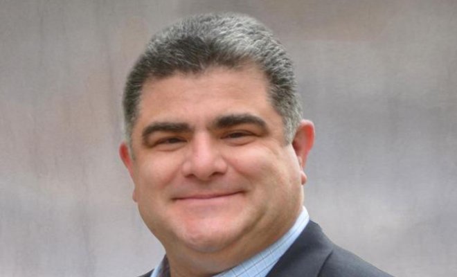 Man is smiling with a black suit on and blue dress shirt.