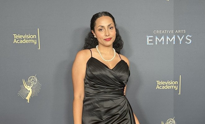 Raciely Rodriguez, in a black evening dress, stands before a backdrop showing Television Academy and Emmy logos.