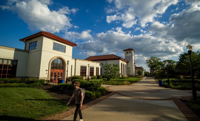 Student walking around campus with clouds in the sky.