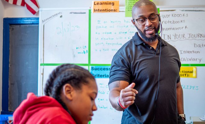 An elementary school teacher speaks to a class as they complete an assignment.