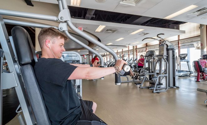A student uses weight lifting equipment in a gym.