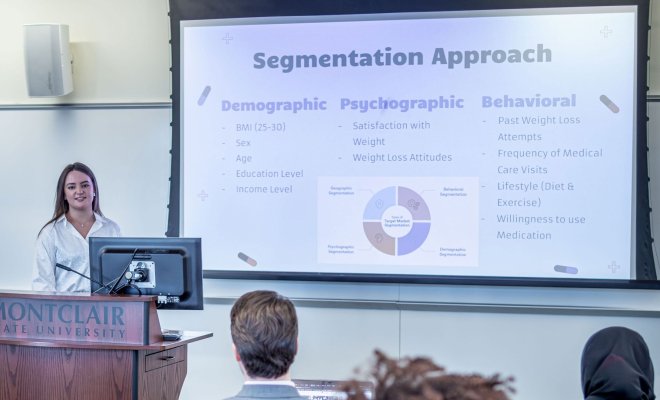 Student presenting in a classroom, standing in front of a projection screen.