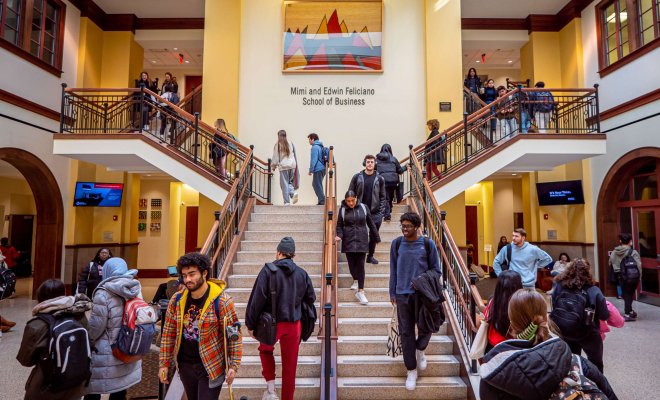 Wide view of the Feliciano School of Business building's lobby with dozens of students going up and down the grand staircase.