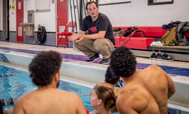 Students in a pool listen to an instructor.