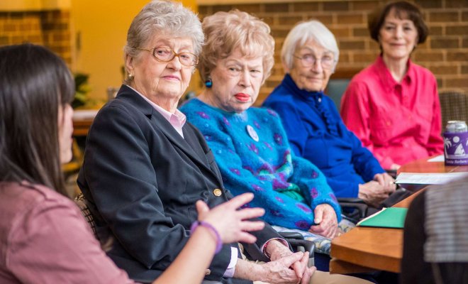 A Montclair student out of focus in the foreground speaks with a group of senior citizens.