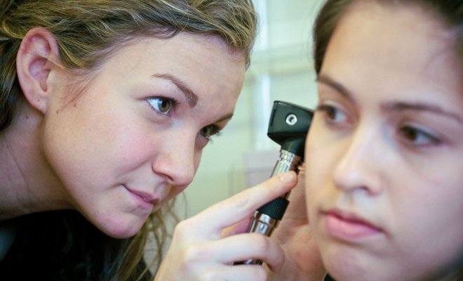 One student looks into another student's ear using an otoscope in a clinic.