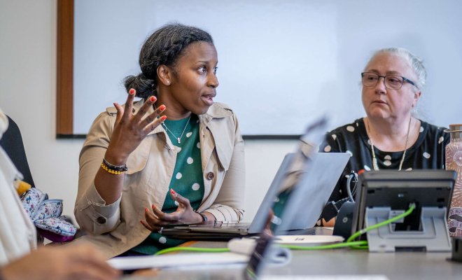 A woman in a group setting speaks to her peers around a conference table.