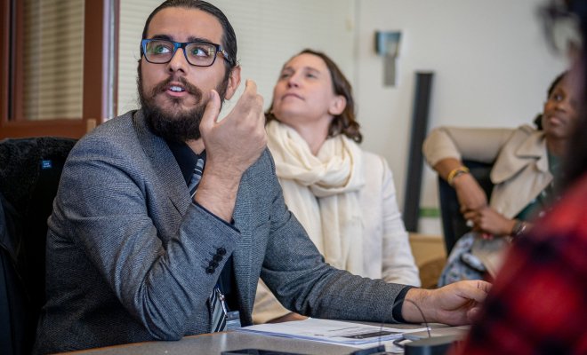 A student wearing a blazer looks up at the projector screen and makes a gesture while asking a question.