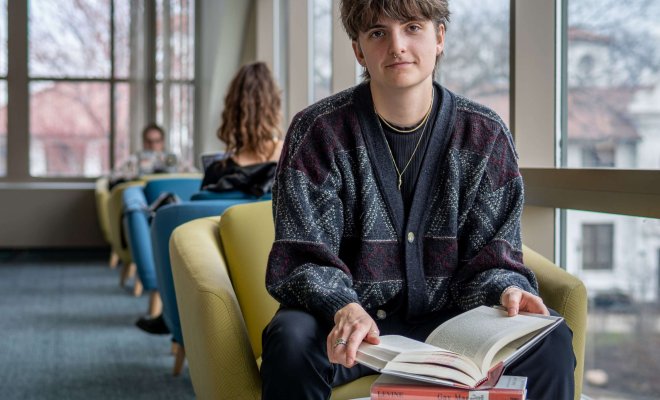 A student sits by the window in the library with a stack of books including Gay Macho by Martin P Levine and The remarkable Rise of Transgender Rights by Jami K Taylor, Daniel C Lewis, and Donald P Haider-Markel