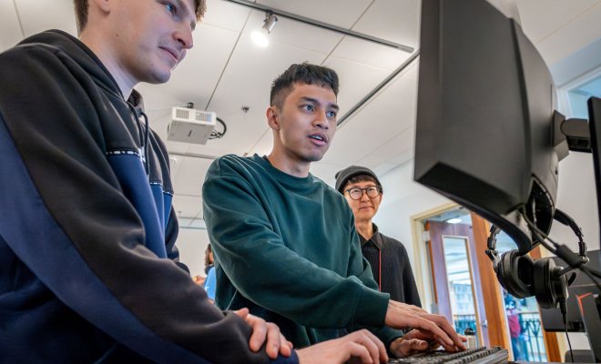 Two students controlling a prototype game using a keyboard while a third looks on