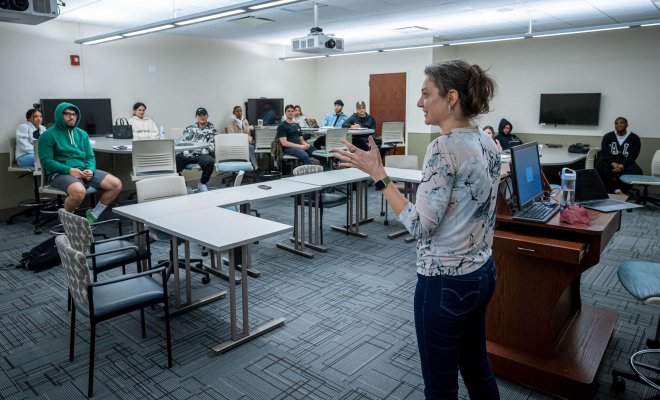 An educator speaks to a group of K-12 students in a classroom setting.