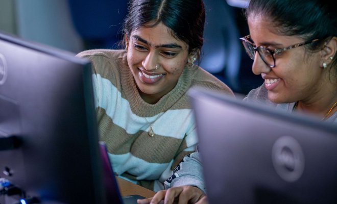 Two students smiling while looking at a computer monitor in a computer lab